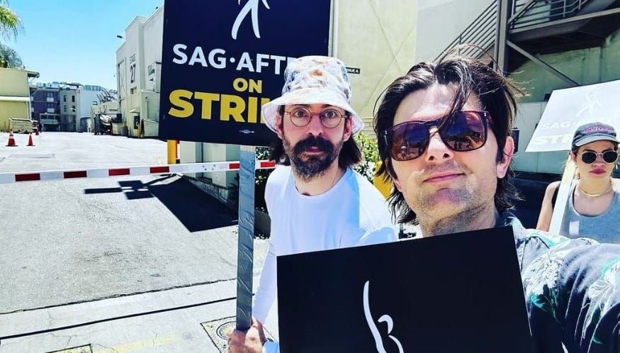 Two men hold protest signs on a picket line in this image from Adam Scott / Instagram