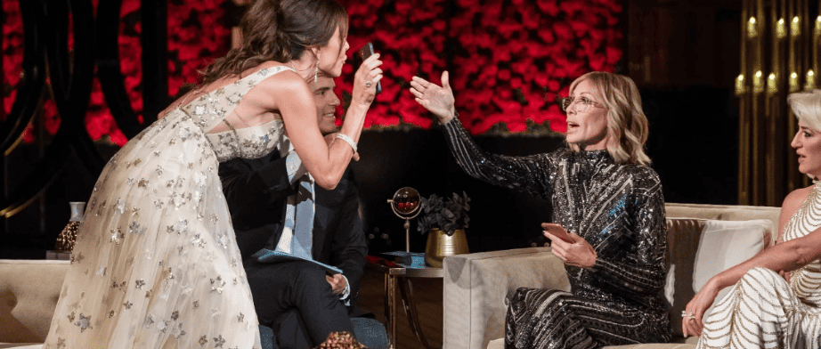 Bethenny Frankel lunges forward to show a screenshot to Carole Radziwill, whose hand is sternly pointed at Bethenny, in the middle of an argument in this image from Ricochet Television